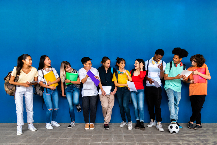 Group of happy multiracial teenage high school students talking and laughing before class wearing backpacks and holding folders.copy space